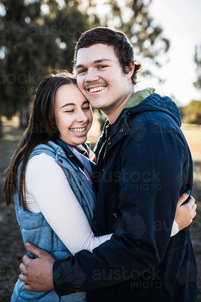 Young couple standing cuddling smiling - Australian Stock Image
