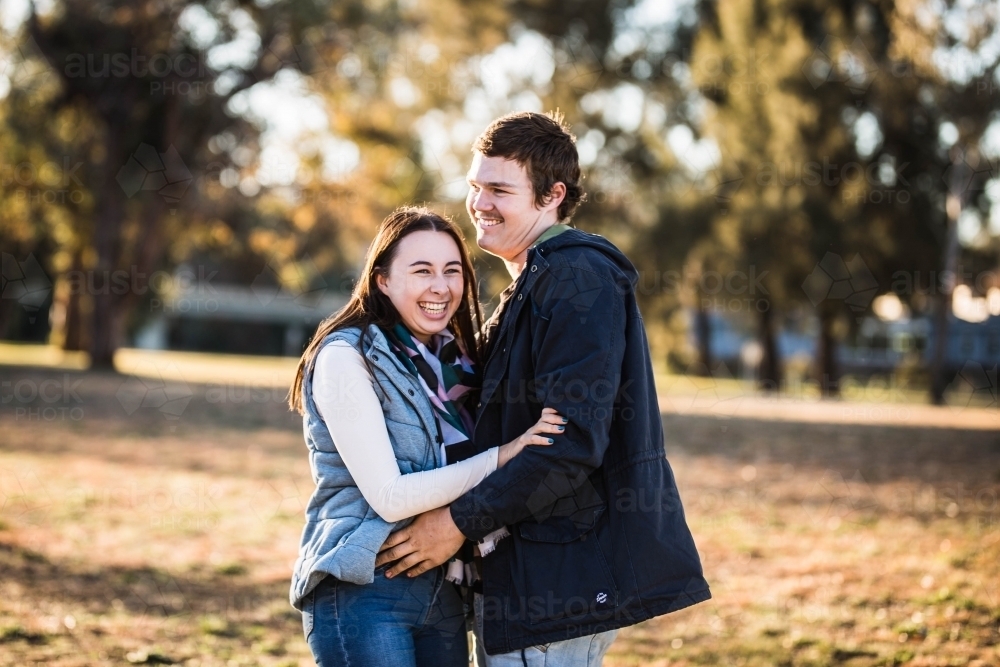 Young couple standing together in park laughing - Australian Stock Image