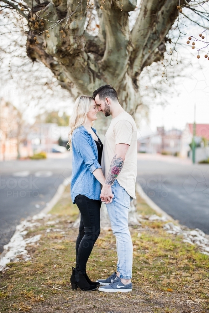 Young couple standing touching foreheads looking at each other holding hands - Australian Stock Image