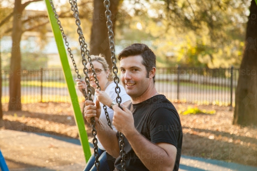 Young couple swinging on swings at the park - Australian Stock Image