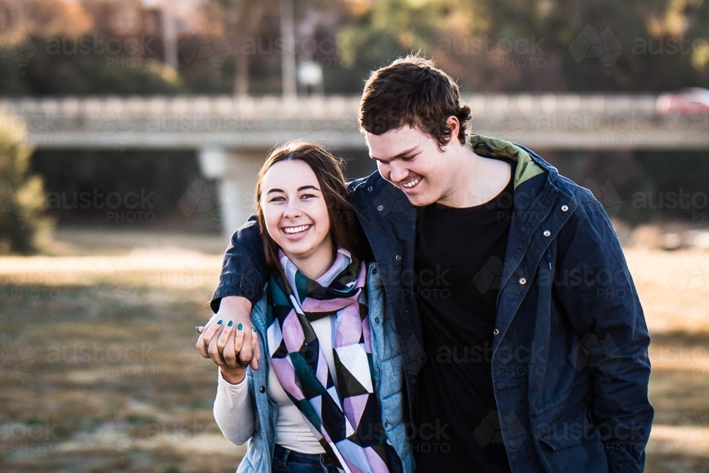 Young couple walking in park holding hands and smiling - Australian Stock Image