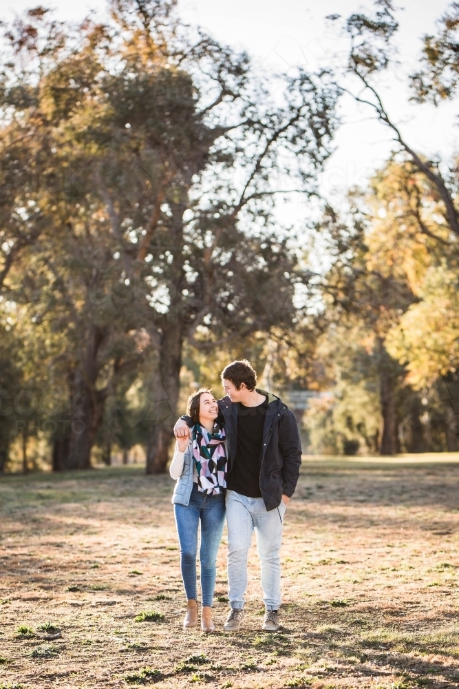 Young couple walking in park holding hands looking at each other - Australian Stock Image