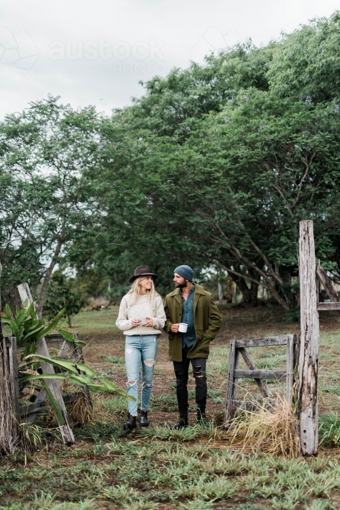 Young couple walking through farm holding cups of coffee - Australian Stock Image