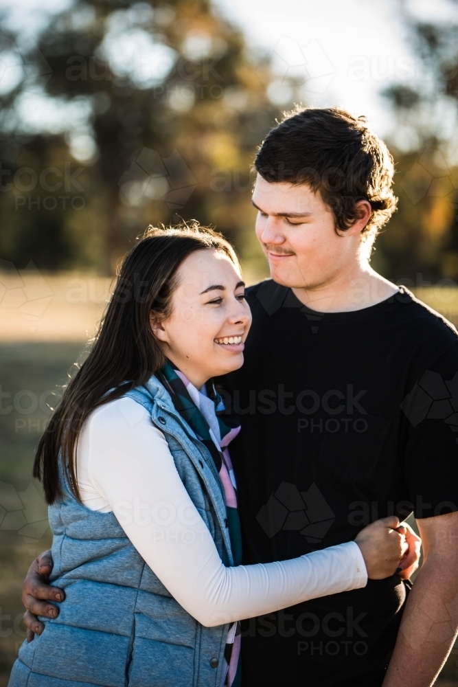 Young couple with arms around each other man looking down at girlfriend smiling - Australian Stock Image