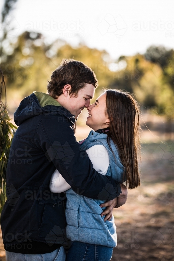 Young couple wrapped in each other's arms smiling noses touching - Australian Stock Image