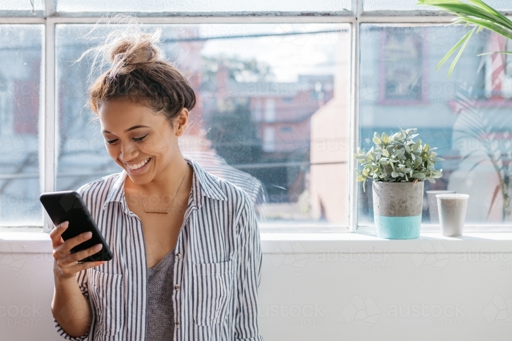 Young creative female smiling and reading her phone at a studio window - Australian Stock Image