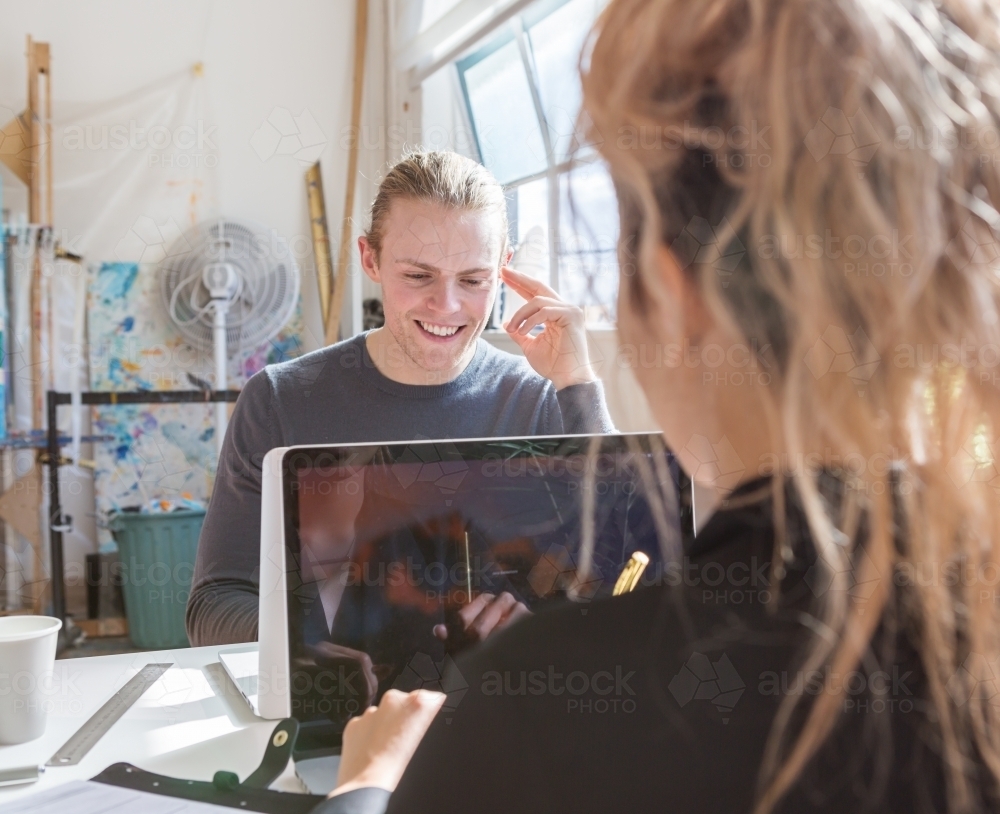 Young creative man smiling at a shared desk at work : Austockphoto Young creative man smiling at a shared desk at work - Australian Stock Image