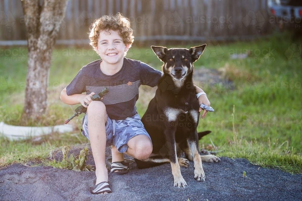 Young curly haired boy with arm around black and tan kelpie dog - Australian Stock Image