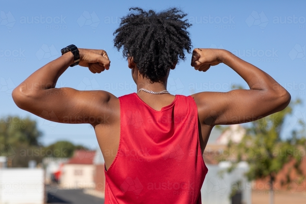 young dark guy from behind flexing muscles outdoors - Australian Stock Image