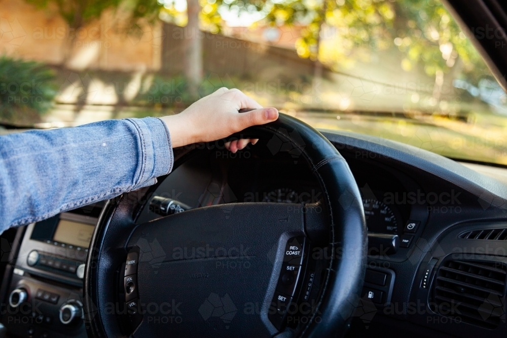 Young driver driving with one hand on the steering wheel or right hand drive car - Australian Stock Image