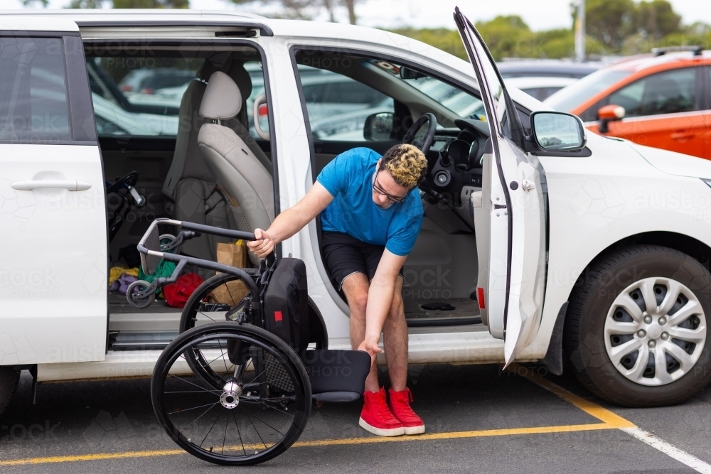 young driver folding wheelchair to put into car - Australian Stock Image