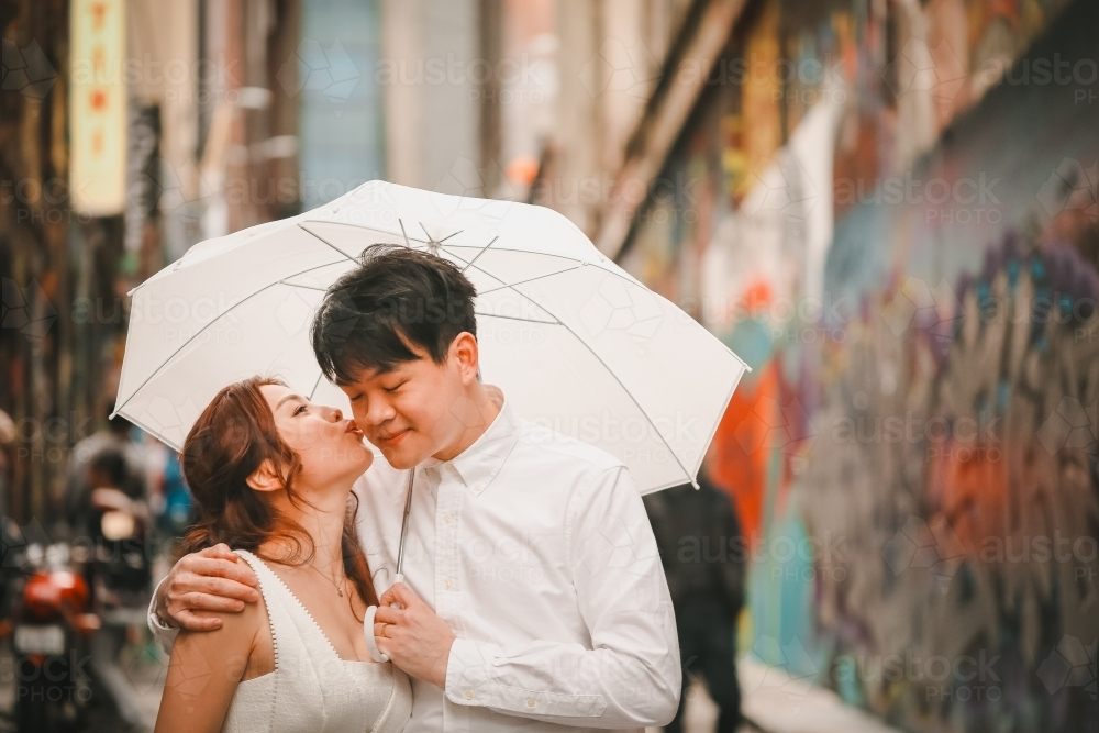Young engaged couple posing with white umbrella in Hosier Lane, iconic graffiti laneway in Melbourne - Australian Stock Image