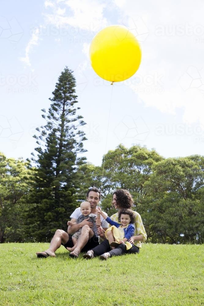 Young family of four on a hill in a park with a large yellow balloon - Australian Stock Image