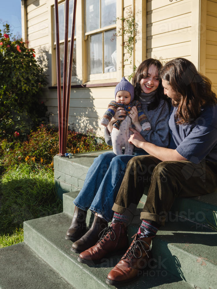 Young family sitting on the steps of their porch on sunny day - Australian Stock Image