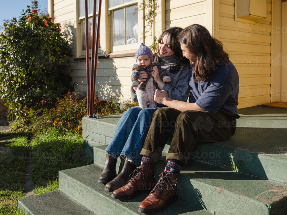 Young family sitting on the steps of their porch on sunny day - Australian Stock Image