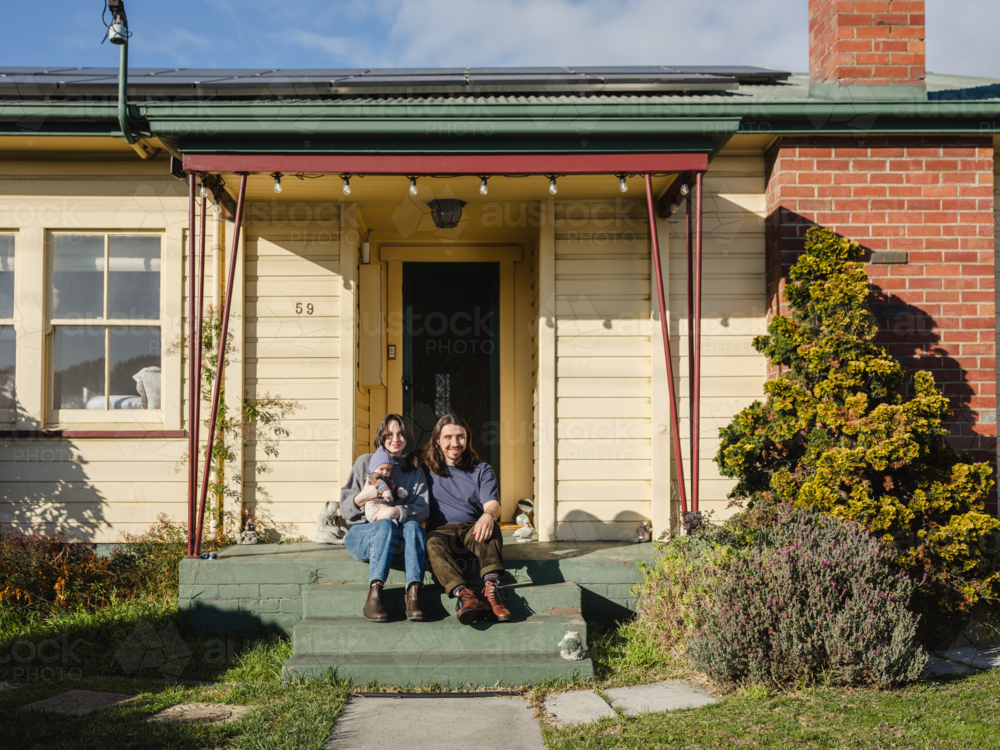 Young family sitting on the steps of their porch on sunny day - Australian Stock Image