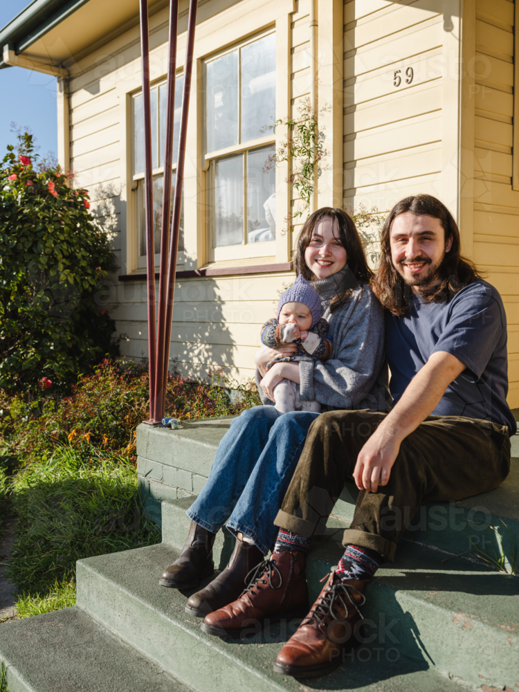 Young family sitting on the steps of their porch on sunny day - Australian Stock Image