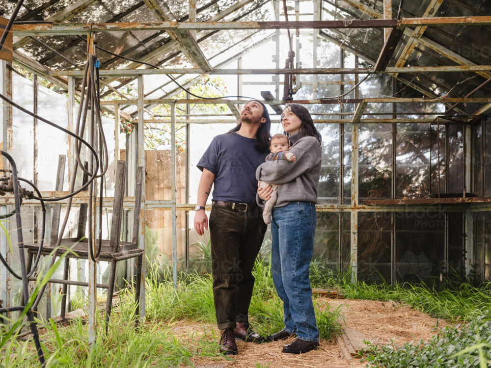 Young family standing inside weathered glasshouse - Australian Stock Image