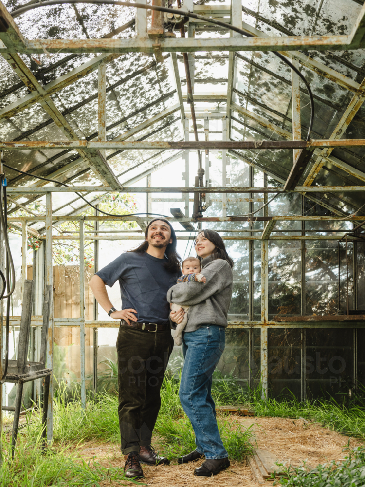 Young family standing inside weathered glasshouse - Australian Stock Image