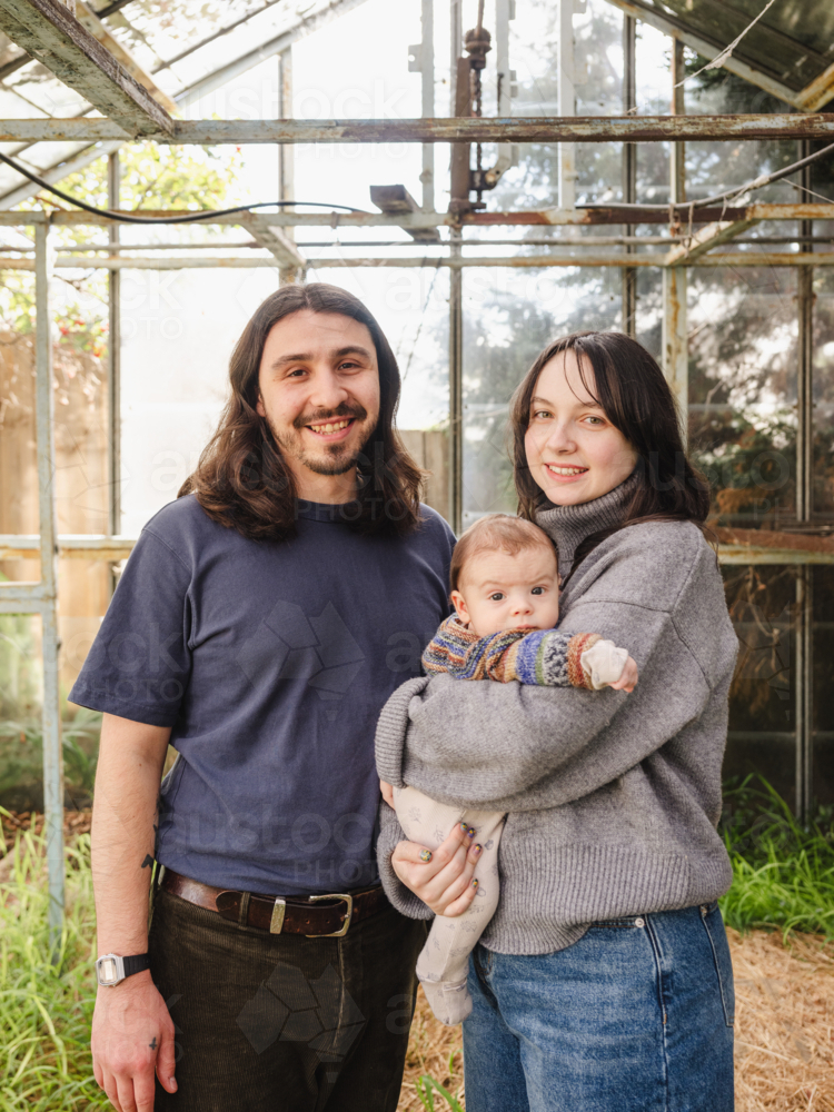 Young family standing inside weathered glasshouse - Australian Stock Image