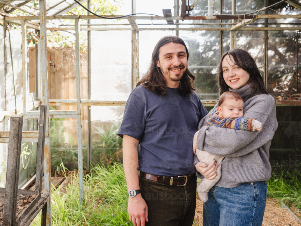 Young family standing inside weathered glasshouse - Australian Stock Image