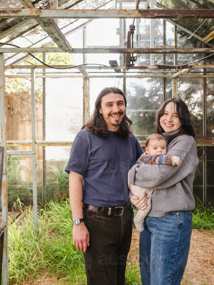Young family standing inside weathered glasshouse - Australian Stock Image