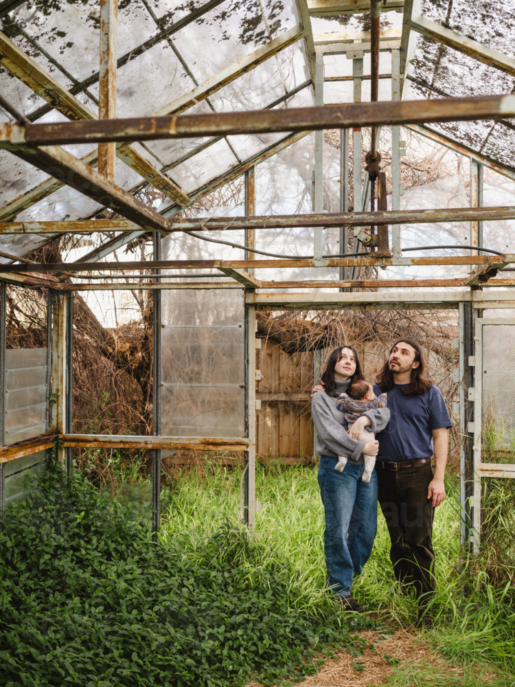 Young family standing inside weathered glasshouse - Australian Stock Image