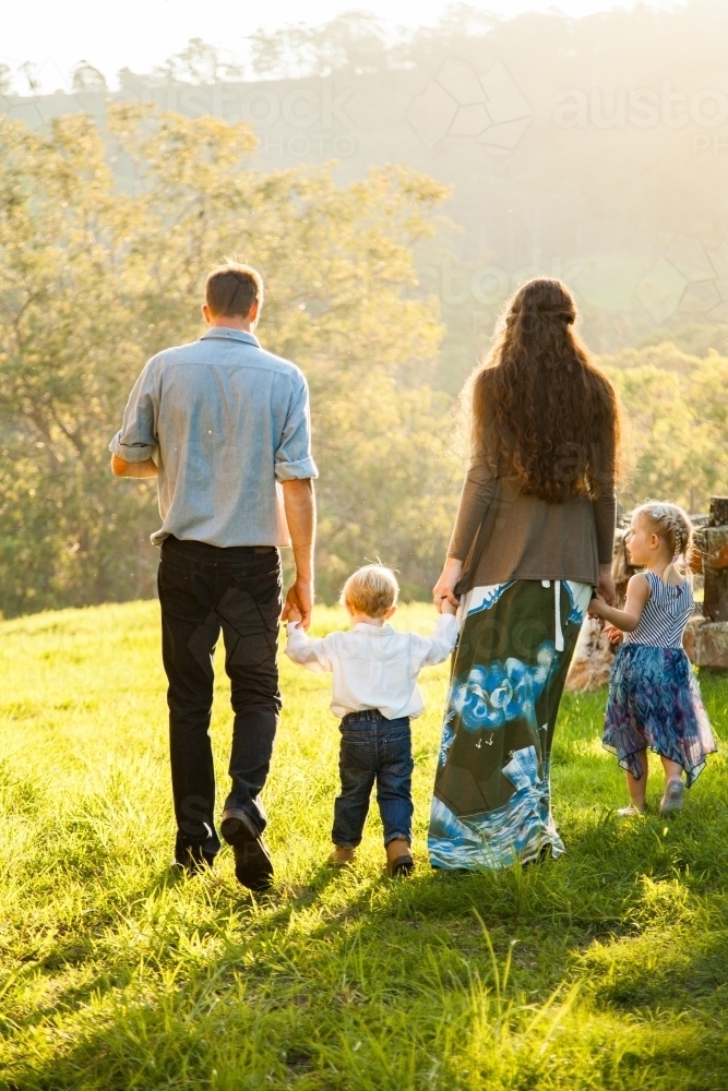 Young family walking away through paddock holding hands - Australian Stock Image
