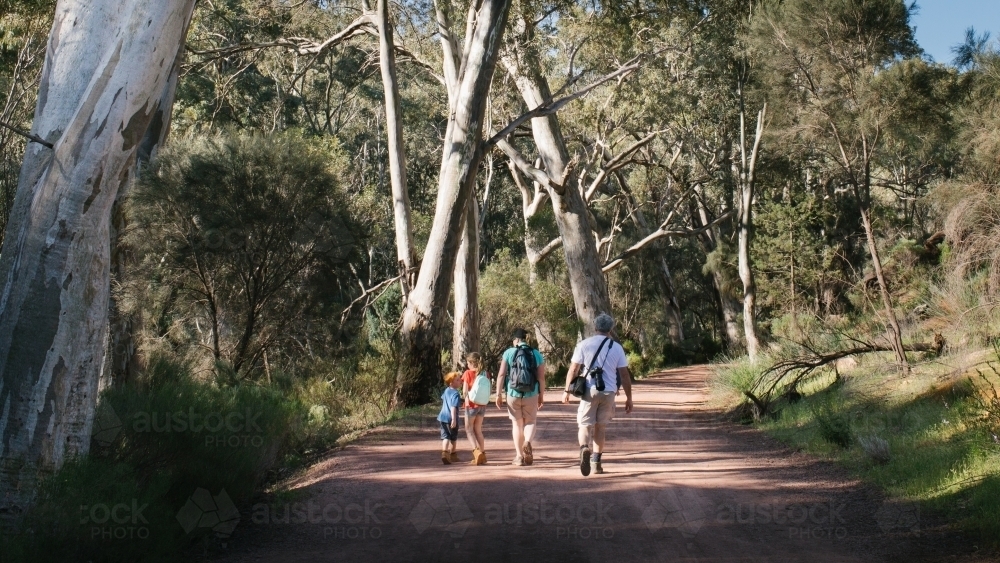Young family walking away up a dirt road from behind - Australian Stock Image
