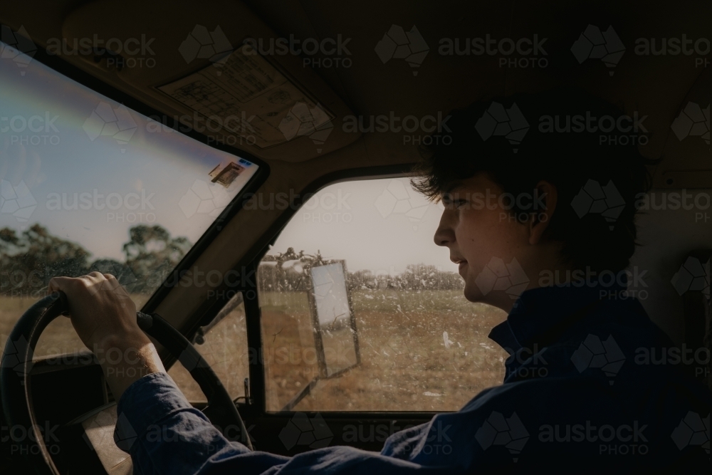 Young Farmer driving the ute through the paddocks in Summer - Australian Stock Image