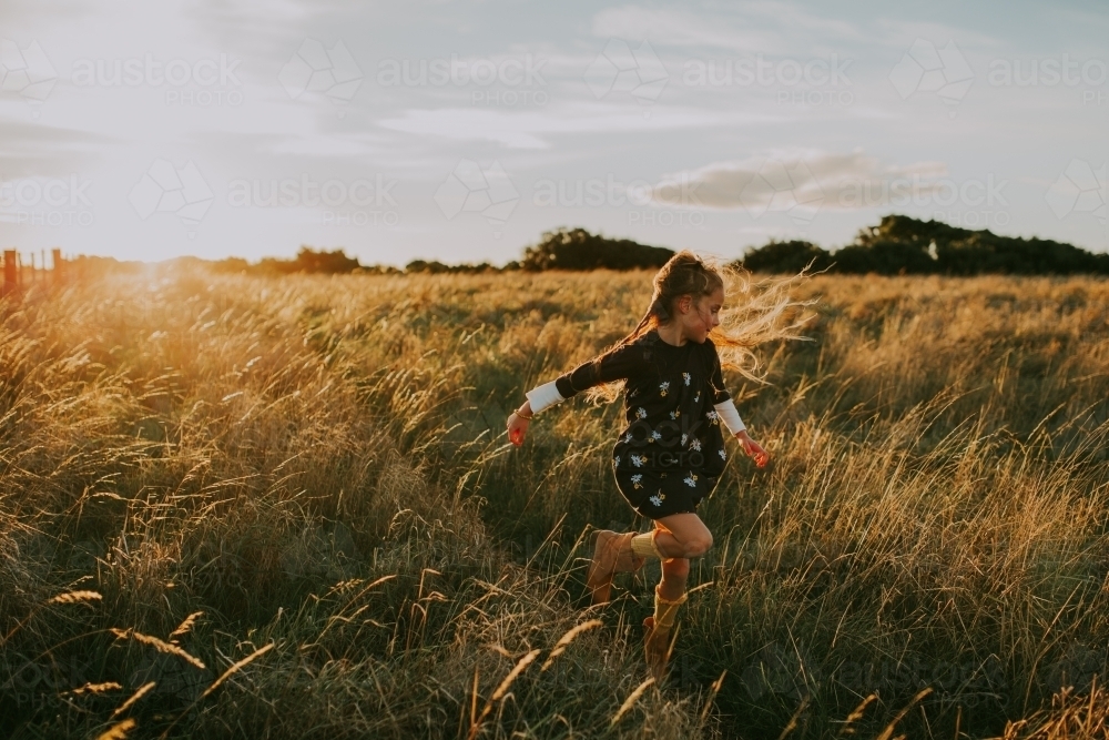 Young fashionable girl running through long grass in paddock at sunset - Australian Stock Image