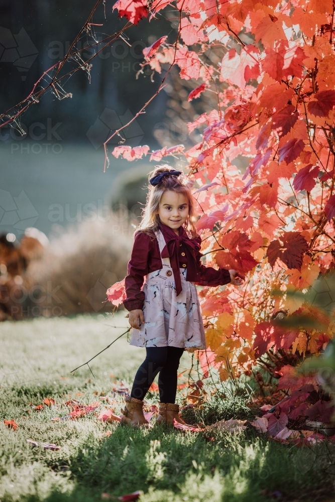 Young fashionable girl standing near autumn leaves smiling - Australian Stock Image