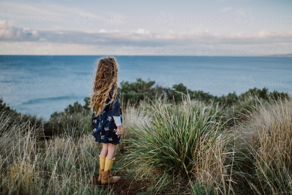 Young fashionable girl standing on a cliff top looking out to the ocean - Australian Stock Image