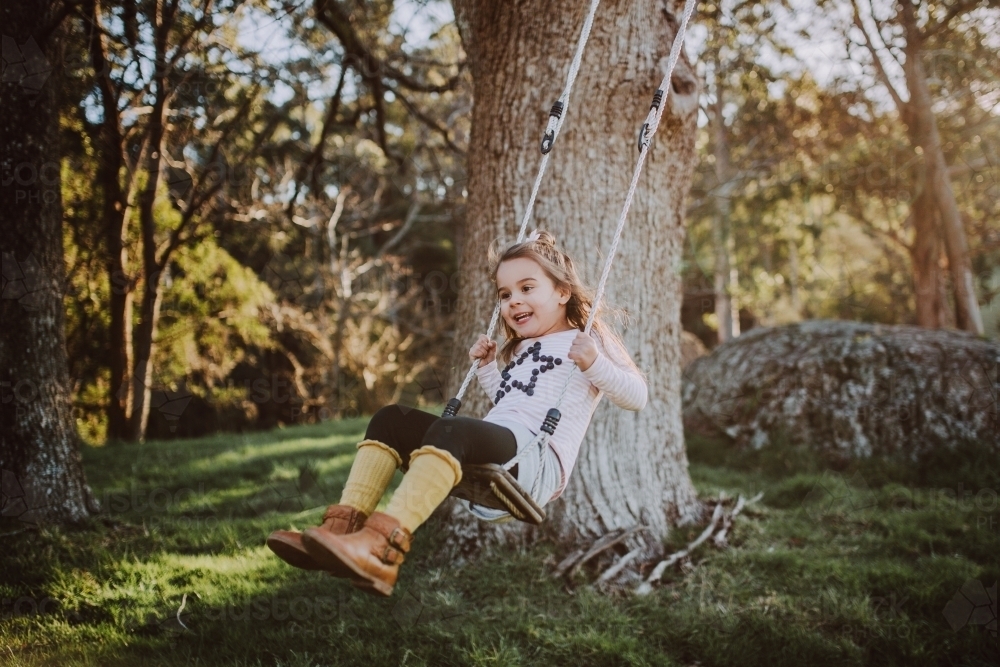 Young fashionable girl swinging on a wooden swing in a farm setting - Australian Stock Image
