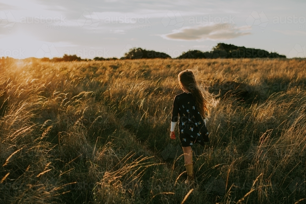 Young fashionable girl walking through long grass in paddock at sunset - Australian Stock Image