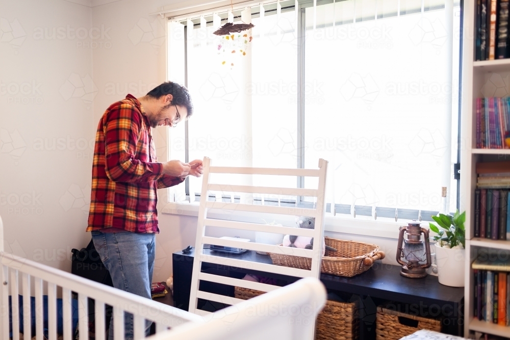 Young father in baby's nursery assembling cot - Australian Stock Image