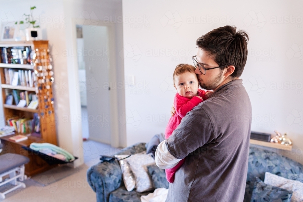 Young father inside home cuddling baby daughter - Australian Stock Image