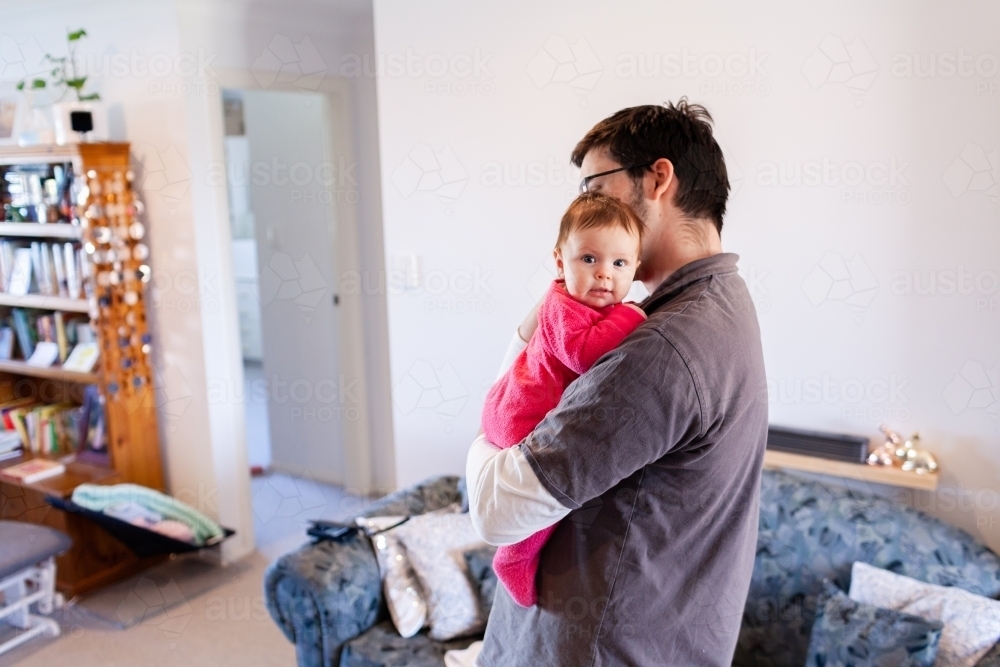 Young father inside home cuddling baby daughter - Australian Stock Image