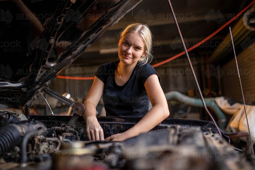 young female australian tradesperson mechanic working on car engine in auto repair garage - Australian Stock Image