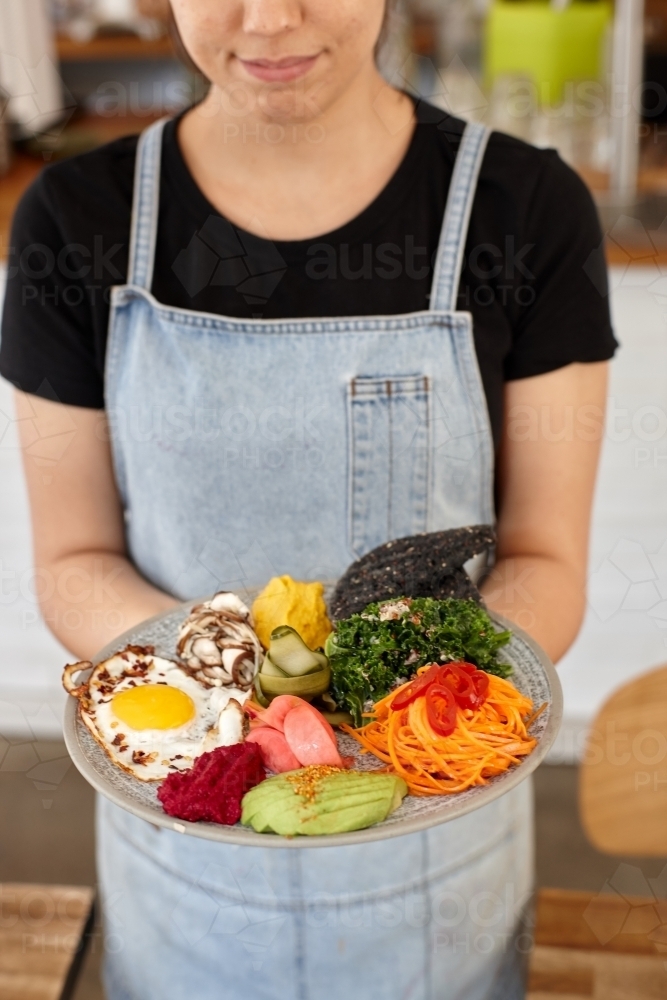 Young female cafe worker holding healthy dish - Australian Stock Image