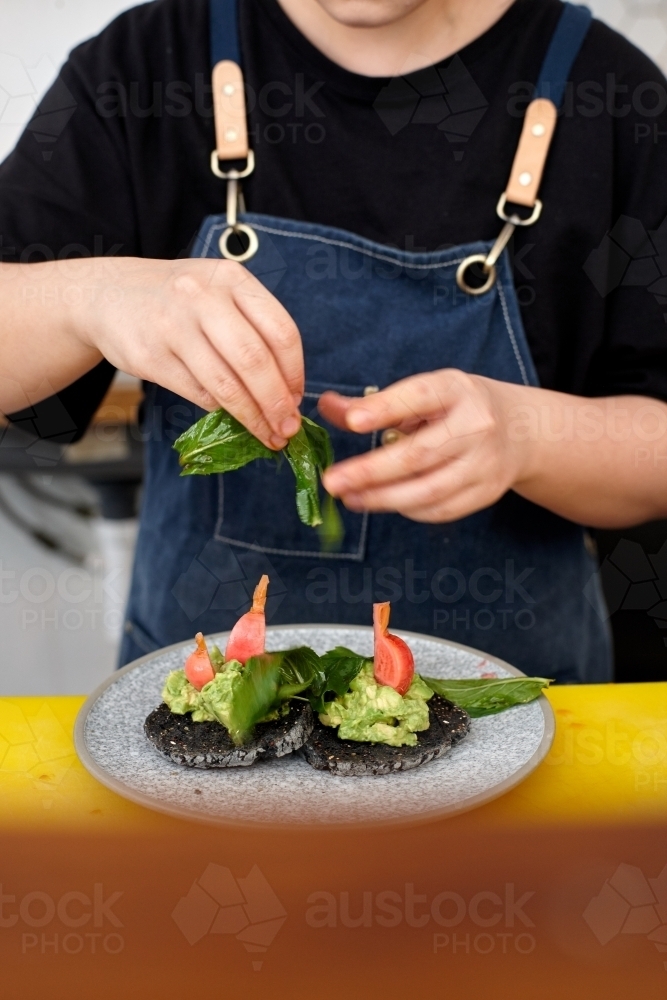Young female chef in cafe kitchen preparing healthy vegetarian meal - Australian Stock Image