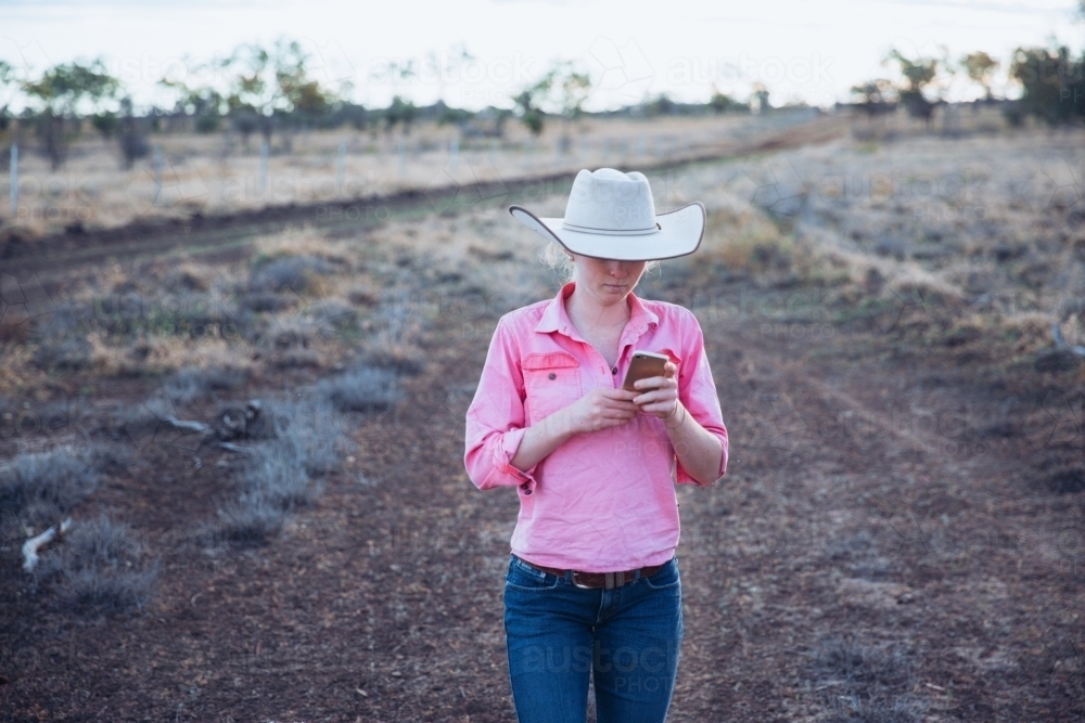 Young female farmer using smart phone in paddock - Australian Stock Image