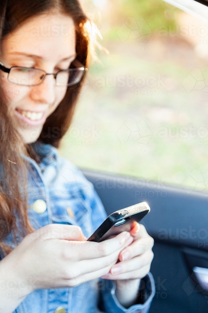 Young female passenger using phone in car - Australian Stock Image