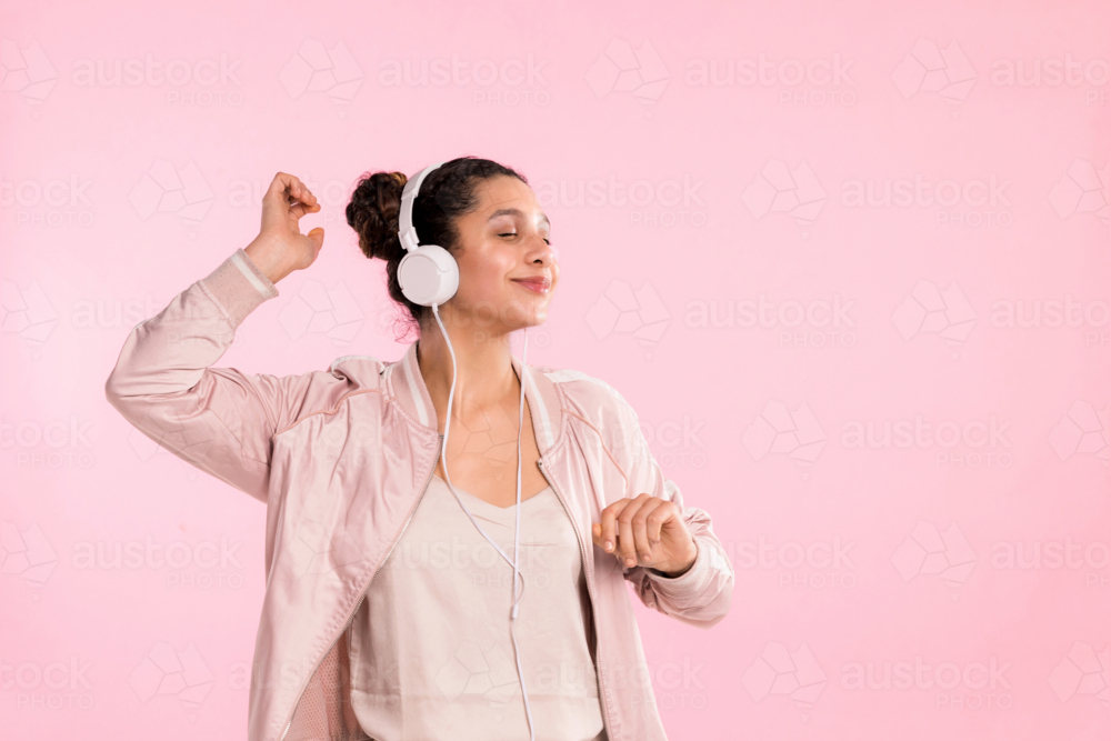 young female person wearing headphones on pink studio backdrop - Australian Stock Image
