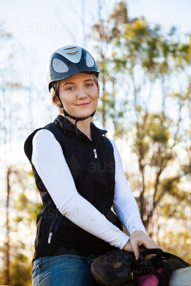 Young female rider on her horse wearing a riding helmet for safety - Australian Stock Image