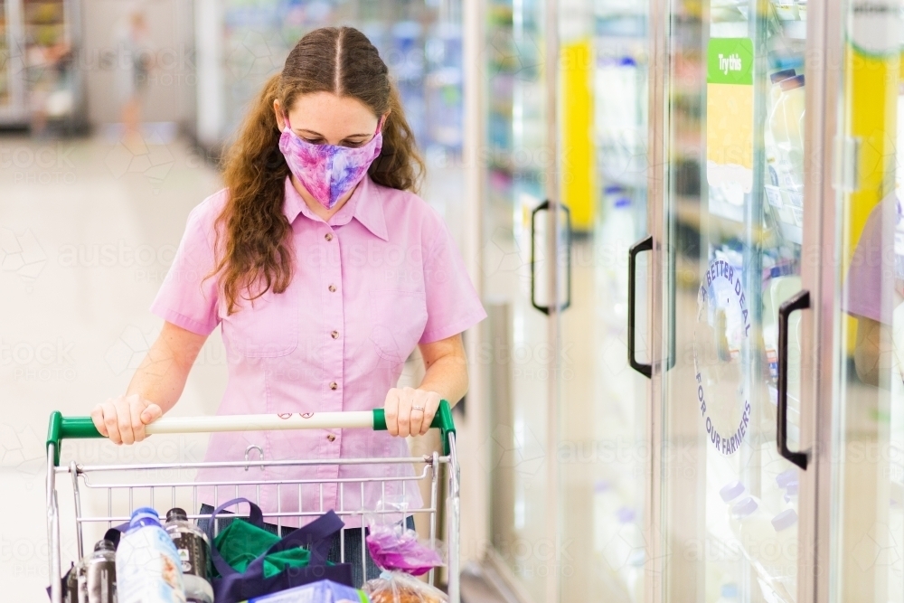 Image of Young female shopper walking down grocery store aisle wearing
