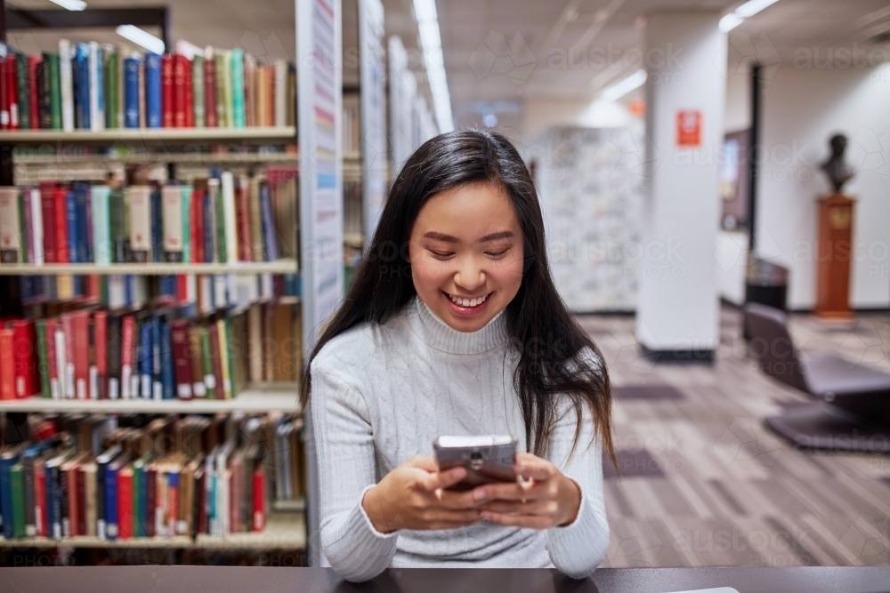 Young female student on her phone at university library - Australian Stock Image