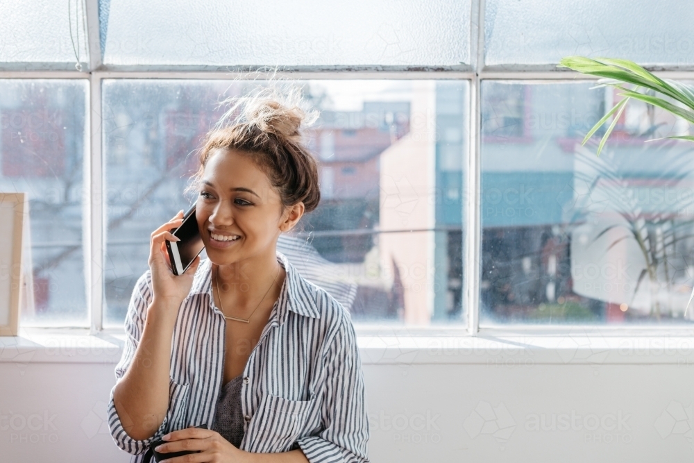 Young female talking on a mobile phone in a bright studio office - Australian Stock Image