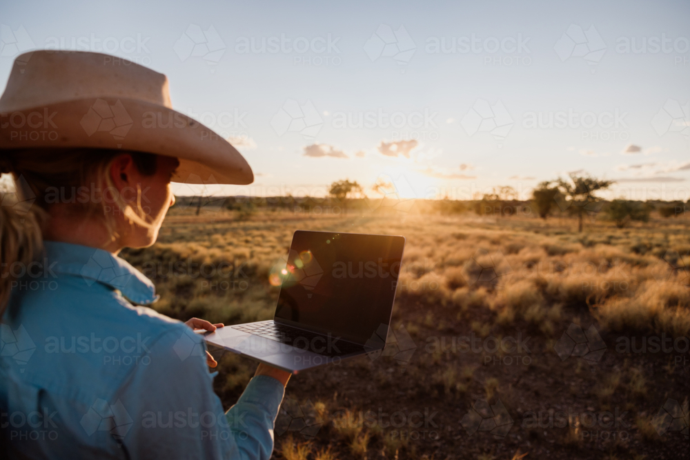 Young female with hat looking at a computer facing a paddock - Australian Stock Image