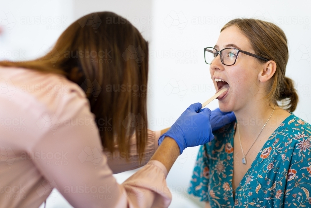 Young female with mouth open being checked by doctor - Australian Stock Image